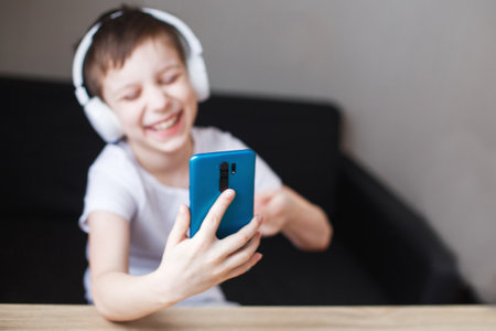 leisure, children, technology and people concept - smiling boy with smartphone and headphones having video call at home. child with mobileの写真素材