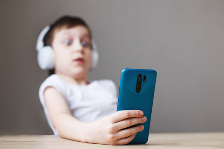 leisure, children, technology and people concept - surprise boy with smartphone and headphones having video call at home. child with mobileの写真素材