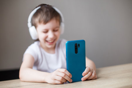 leisure, children, technology and people concept - smiling boy with smartphone and headphones having video call at home. child with mobileの写真素材