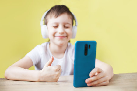 leisure, children, technology and people concept - smiling boy with smartphone and headphones having video call at home. child with mobile on a yellow background. young bloggerの写真素材
