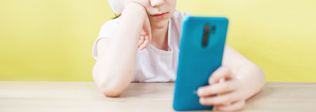 leisure, children, technology and people concept - smiling boy with smartphone and headphones having video call at home. child with mobile on a yellow background. young blogger .bannerの写真素材
