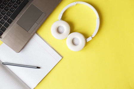 Top view open notepad, headphones pen and a laptop on yellow background. workplaceの写真素材