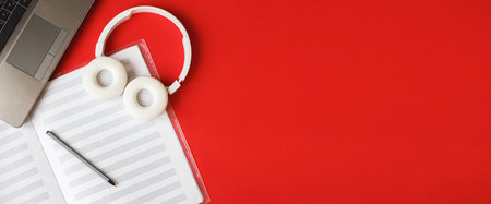 Top view open music book, headphones pen and a laptop on red background. workplace. bannerの写真素材