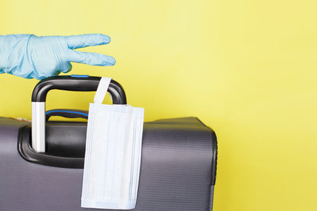 Hand with a luggage bag and medical mask isolated on a yellow background. protectionの写真素材