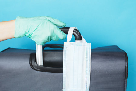 Hand with a luggage bag and medical mask isolated on a blue background. protection disease  infection.の写真素材