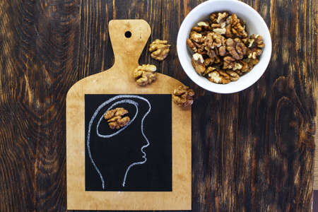 drawn person head with brain and nuts walnuts on wooden background. Concept of healthy food for a human to think.の写真素材