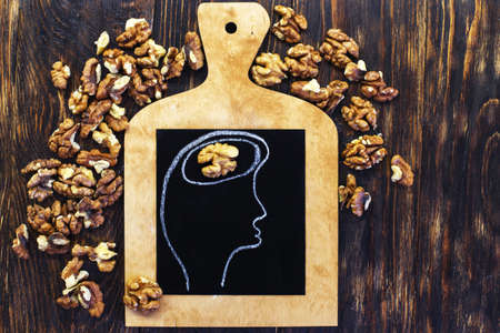drawn person head with brain and nuts walnuts on wooden background. Concept of healthy food for a human to think.の写真素材