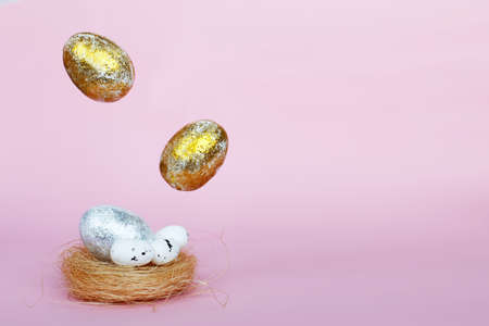 Gold and silver Easter eggs levitation to the nest on a pink background. Easter concept. Copy spaceの写真素材