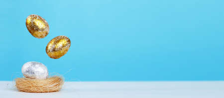 Gold and silver Easter eggs levitation to the nest on a blue background. Easter concept. Copy space. bannerの写真素材