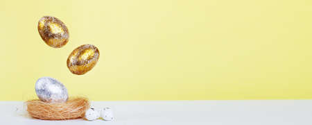 Gold and silver Easter eggs levitation to the nest on a yellow background. Easter concept. Copy...