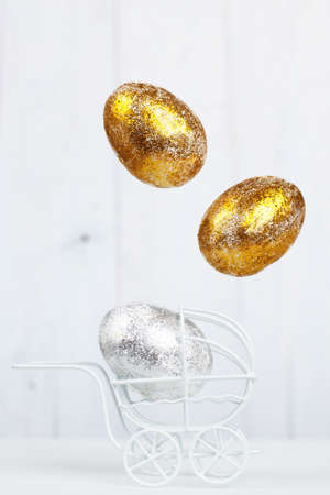 Easter golden and silver eggs levitation in the white baby stroller on a light wooden background. Newborn conceptの写真素材