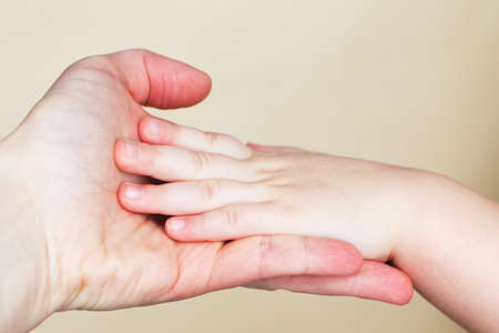 Close up of mothers hand holding babies hand. Isolated on a beige background.の写真素材
