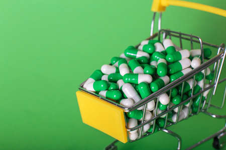 Shopping cart with medical pills on green backgroundの写真素材
