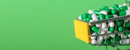 Shopping cart with medical pills on green background. bannerの写真素材