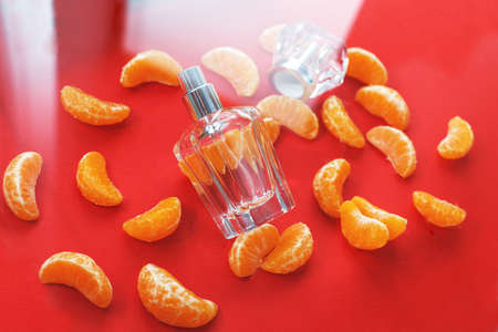 perfume bottle for women with citrus notes on a red background, decorated with Mandarin slices. The concept of a fresh citrus perfume or aromatherapy, fruity aromas.の写真素材