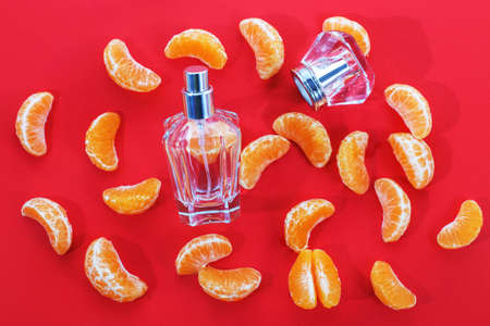 perfume bottle for women with citrus notes on a red background, decorated with Mandarin slices. The concept of a fresh citrus perfume or aromatherapy, fruity aromas.の写真素材