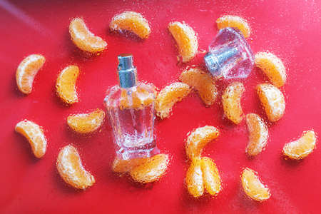 perfume bottle for women with citrus notes on a red background, decorated with Mandarin slices under drops of water. The concept of a fresh citrus perfume or aromatherapy, fruity aromas.の写真素材