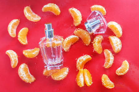perfume bottle for women with citrus notes on a red background, decorated with Mandarin slices under drops of water. The concept of a fresh citrus perfume or aromatherapy, fruity aromas.の写真素材