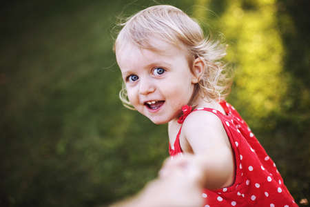 portrait of a little happy girl. the child holds the hand of a parent and playsの写真素材