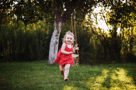 happy baby smiling. a little girl running in the garden at sunset outdoor barefootの写真素材