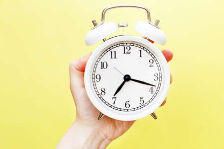 female holding white alarm clock in her hand on a yellow backgroundの写真素材