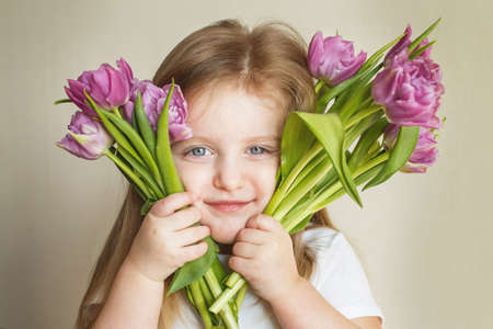 portrait of a happy smiling litlle girl with bouquet of flowers tulips in her handsの写真素材