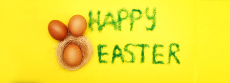 inscription happy easter from grass with bunny eggs and nest on a yellow background. copy space for...