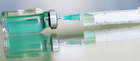 Vial filled with liquid vaccine in medical lab with syringe. medical ampoule and syringe on the glass surface. bannerの写真素材