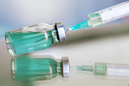 Vial filled with liquid vaccine in medical lab with syringe. medical ampoule and syringe on the glass surfaceの写真素材