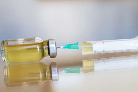 Vial filled with liquid vaccine in medical lab with syringe. medical ampoule and syringe on the glass surfaceの写真素材