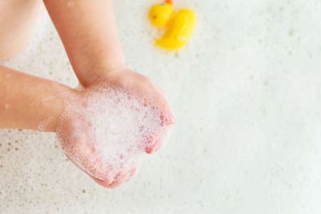 little baby girl playing with foam in a bath tub. Child playing with a toy rubber duck in the...
