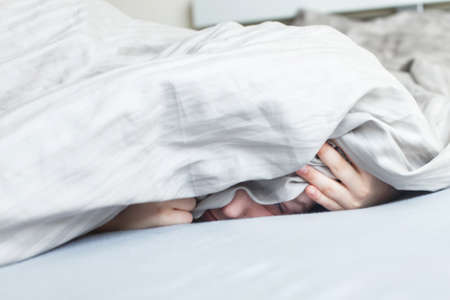 boy in the bed in the morning. the child lies and covers his face with a blanketの写真素材