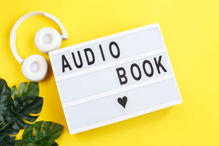 the inscription audiobook on a light box with modern white headphones on a yellow background. Listening to a book. E-learning.の写真素材