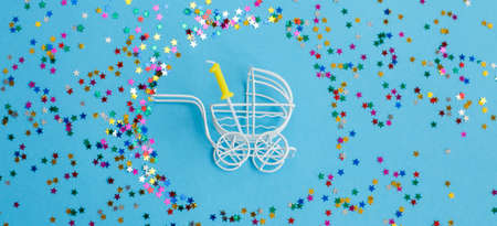 One year birthday party .baby stroller with a candle in the form of the number one on a blue background with stars confetti sequins. bannerの写真素材