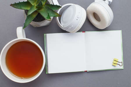 Workplace with a notepad, headphones, a cup of tea or coffee and green plant. Freelancer working space on gray background. Top view.の写真素材