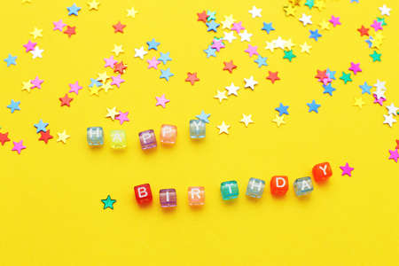 inscription happy birthday and multicolored confetti in the form of stars on a yellow backgroundの写真素材