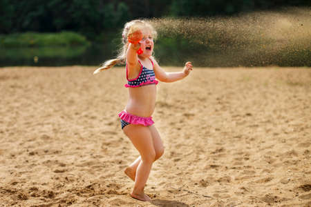 The girl throws the sand up with her hands. Beautiful girl playing with sand on beach. a child having fun relaxing. vacation happiness and freedom concept.の写真素材