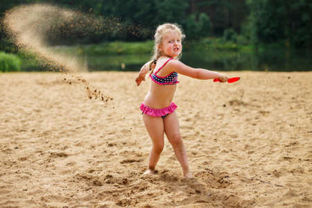 The girl throws the sand up with her hands. Beautiful girl playing with sand on beach. a child having fun relaxing. vacation happiness and freedom concept.の写真素材