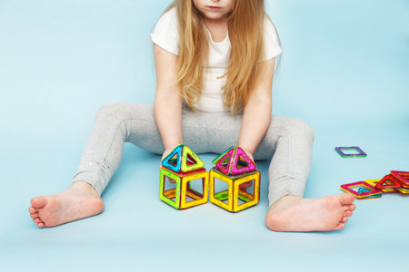 Little girl playing with colorful magnetic constructor toy on a blue background. child built a houseの写真素材
