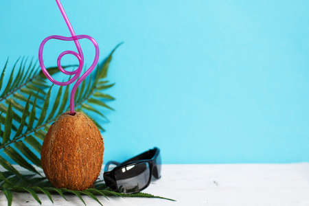 A coconut with straw and black sunglasses on a blue background. Summer and trave concept. copy spaceの写真素材