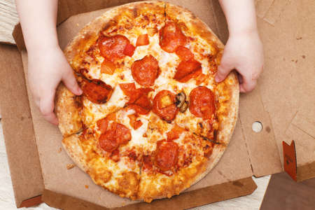 children's hands hold pizza in a cardboard boxの写真素材