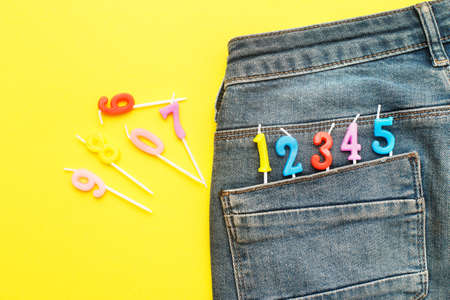 birthday candles sticking out of the back pocket of blue jeans on a yellow background. Number 0-9の写真素材