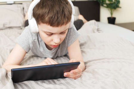 child boy lying on bed at home with pc tablet and reading online or learning or listening to music...