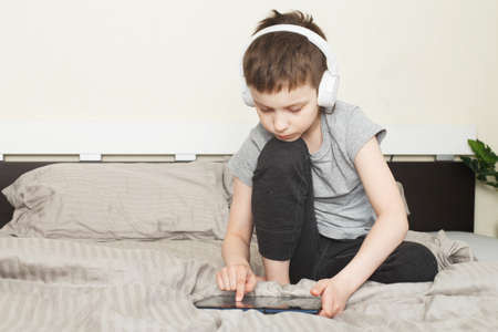 child boy sitting on bed at home with pc tablet and reading online or learning or listening to music...