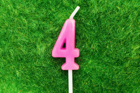 candle in the form of number four on the green grass background, a place for a greeting textの写真素材