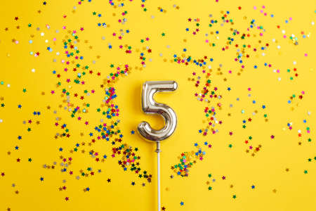 five years birthday party. number five with a multicolored confetti in the form of stars on a yellow backgroundの写真素材
