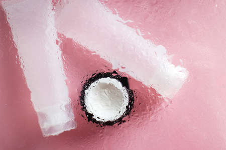 Concept of natural moisturizing skin care products. Face and hand cream under a glass surface with water on a pink background.の写真素材