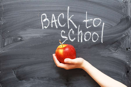 child's hand holding an apple near a chalkboard. Back to school concept backgroundの写真素材