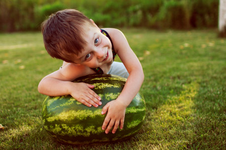 portrait of a happy child boy with a large whole watermelon in the back yardの写真素材