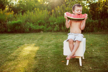 happy smiling child boy eating watermelon outdoor in the backyardの写真素材